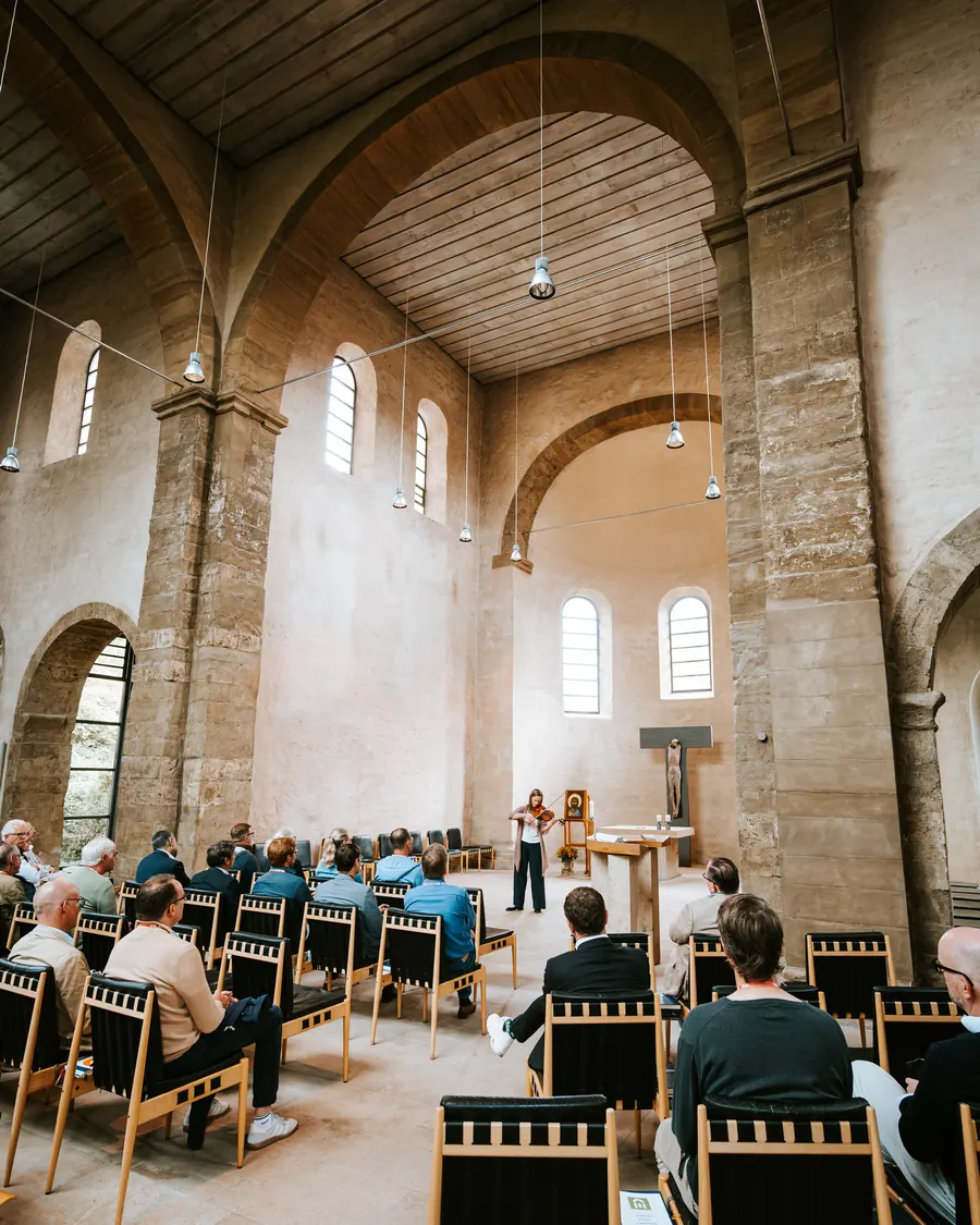Blick in die Klosterkirche mit ihren romanischen Bögen. Vorn spielt eine Geigerin, das Publikum hört zu.