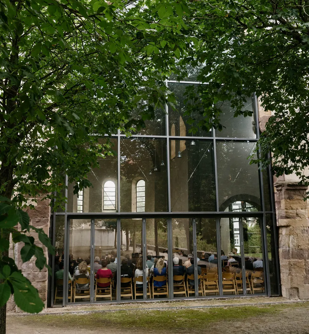 Blick durch Bäume auf die verglaste Front der Klosterkirche Volkenroda
