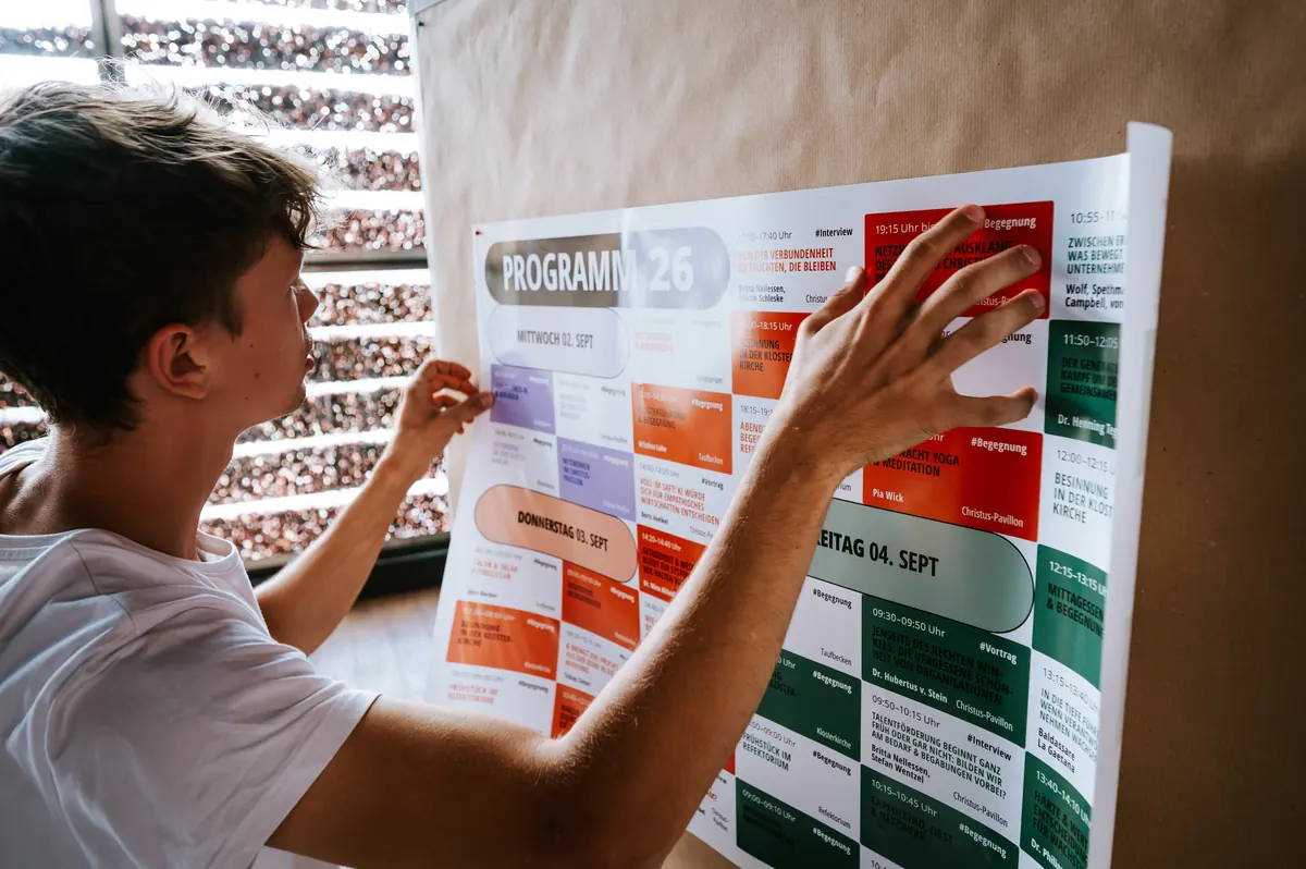 Ein junger Mann hängt das Programmplakat der Konferenz auf
