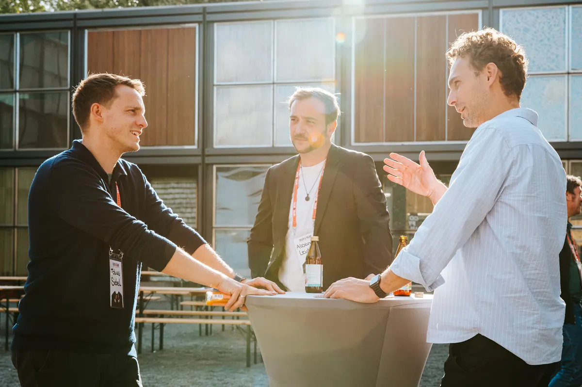 Drei Männer im Gespräch an einem Stehtisch in der Sonne